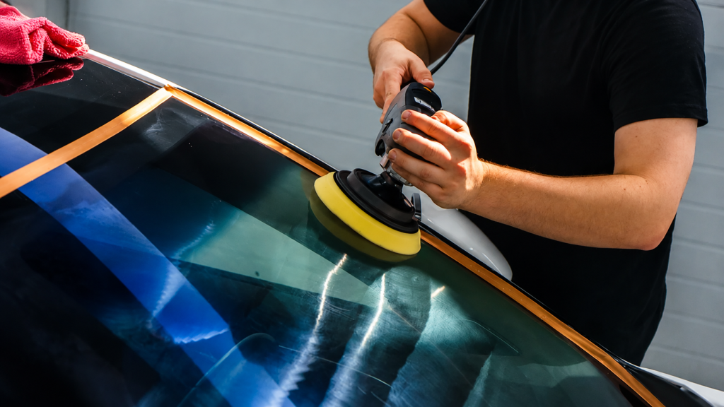Car windshield being polished with a machine buffer.